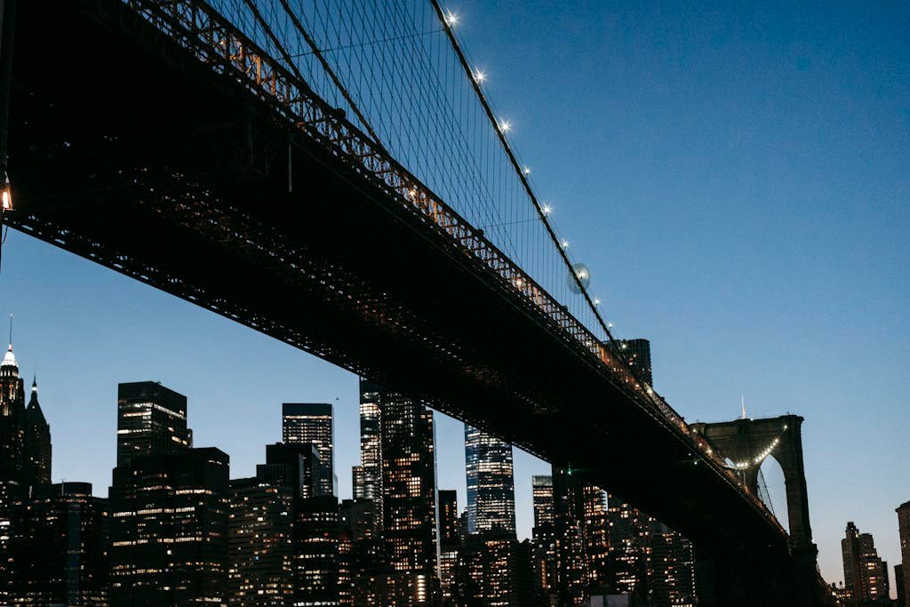 From below of massive suspension bridge against center of city with illuminated high rise buildings