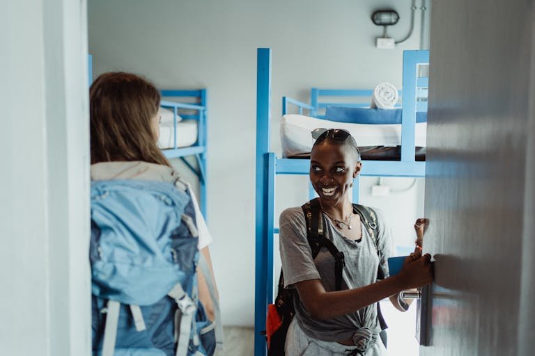 Women Walking into Their Hostel Room with Bunk Beds and Smiling 